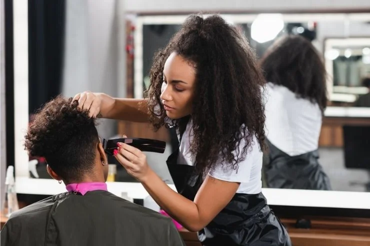 A woman trimming a client's hair with clippers